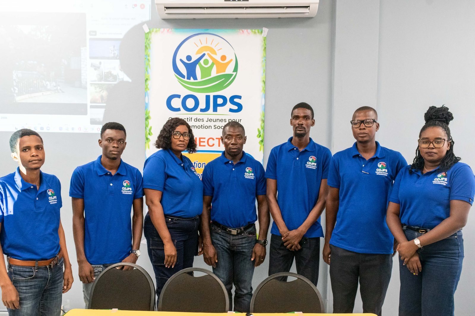 Une équipe du COJPS en polo bleu devant la bannière du collectif
